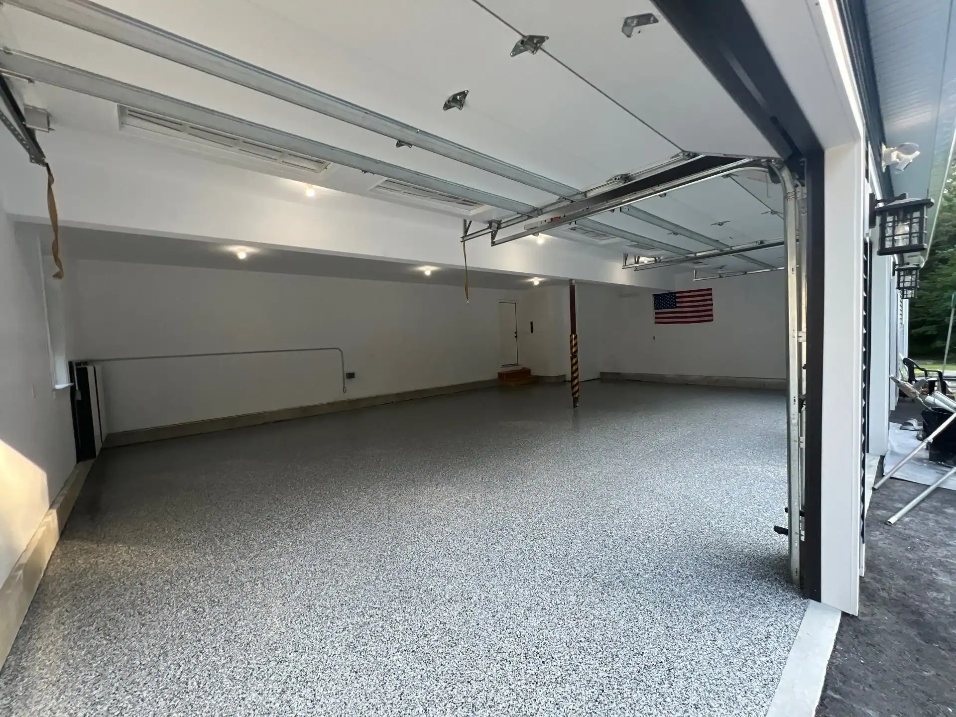 A clean, spacious garage with epoxy flooring in Hartford, CT, features white walls, overhead lighting, and an American flag on the far wall. The open doors let in daylight&mdash;perfect for homes in Middlesex & New London County.