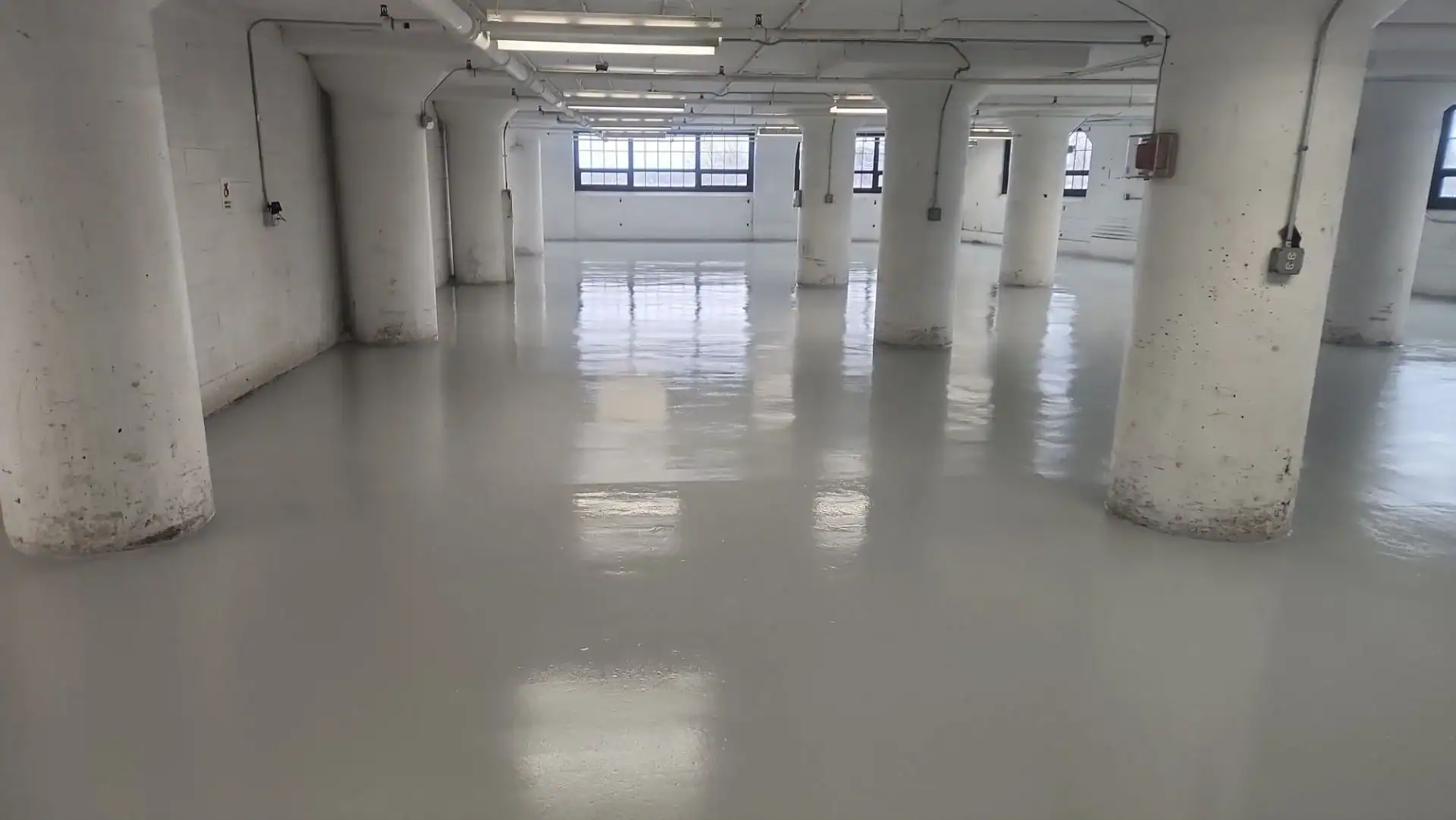 A large, empty industrial room with white walls, tall round columns, large windows, and a shiny, freshly painted epoxy flooring&mdash;ideal for businesses in Hartford and throughout Middlesex & New London County, CT.