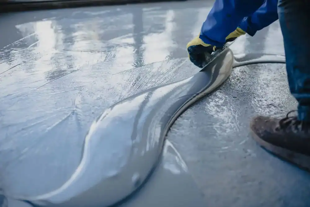 A person wearing gloves smooths out freshly poured concrete or self-leveling floor compound with a trowel, creating an even surface for epoxy flooring in Hartford, New Haven, Middlesex & New London County.