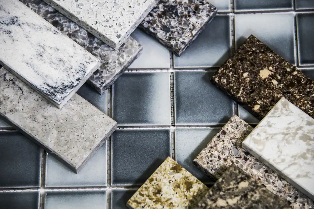 Rectangular samples of various granite and stone countertop materials are arranged on glossy square ceramic tiles in shades of blue-gray, white, brown, and beige&mdash;perfect inspiration for kitchens or epoxy flooring Hartford, CT and New Haven residents will love.