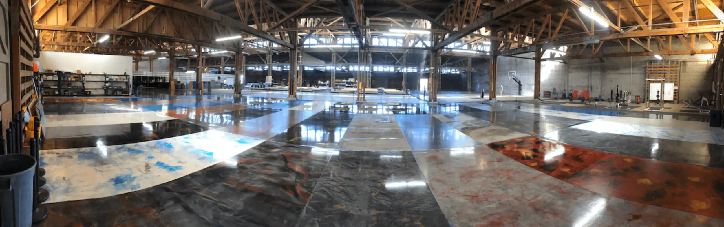 A spacious warehouse with high wooden ceilings, filled with large, colorful, patterned floor panels&mdash;perfect for epoxy flooring Hartford projects; shelves and equipment line the walls in this New Haven-inspired space.