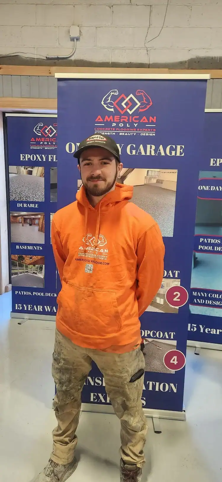 A man wearing an orange hoodie and a cap stands indoors in front of "American Poly Concrete Coating" banners, featuring information about epoxy flooring Hartford and concrete coatings for Middlesex & New London County, and New Haven.