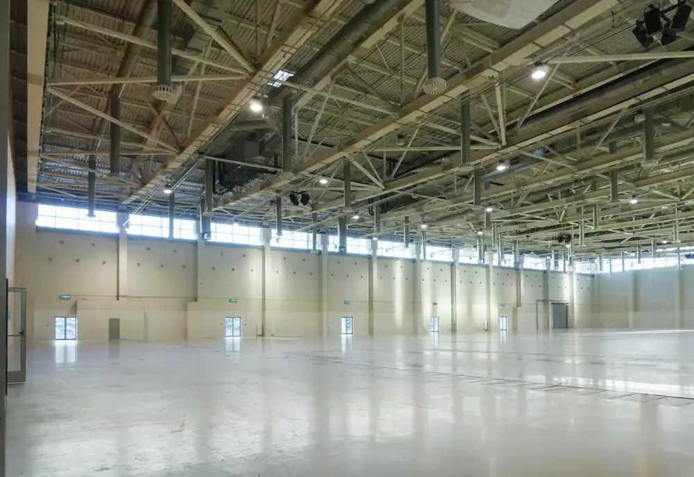 A large, empty industrial hall with high ceilings, exposed beams, and bright lighting. Several doors line the beige walls, and tall windows let in daylight near the ceiling. The polished epoxy flooring gives a clean, spacious look reminiscent of Hartford, CT spaces.