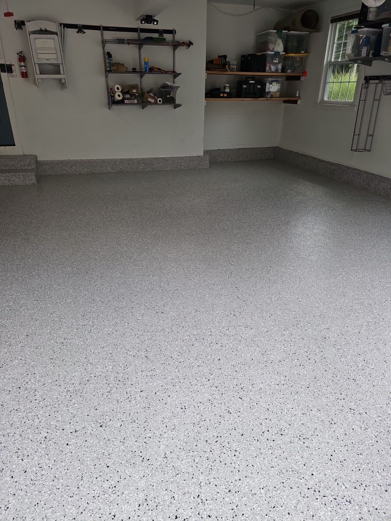 A clean, empty garage with speckled gray epoxy flooring and shelves neatly organizing storage items.