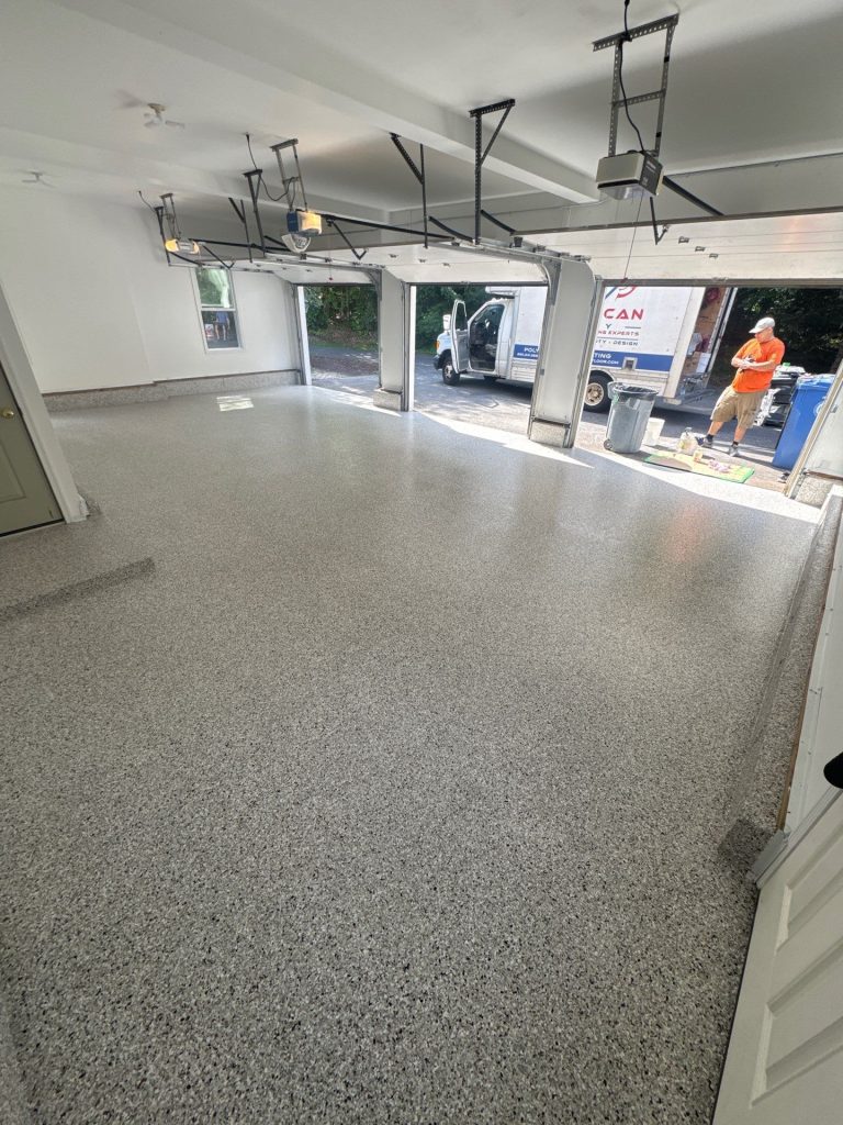A freshly coated garage floor with open doors reveals a person and a truck just outside the clean space.