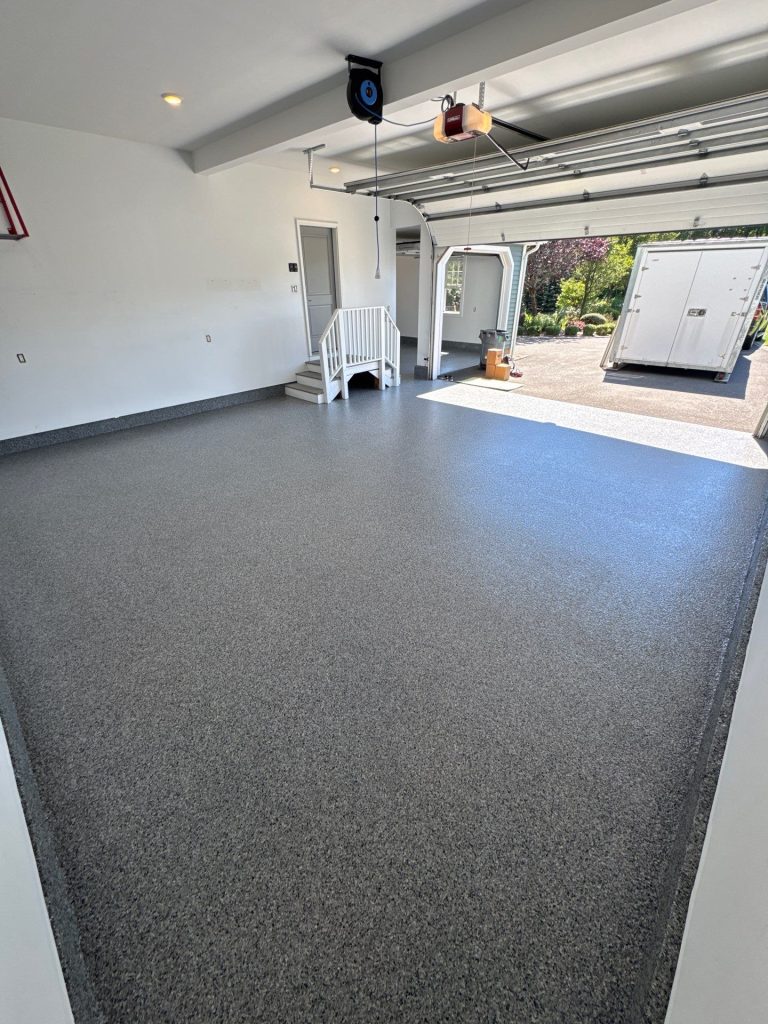 A clean epoxy garage floor, white walls, open door, and a trailer parked outside create a neat look.