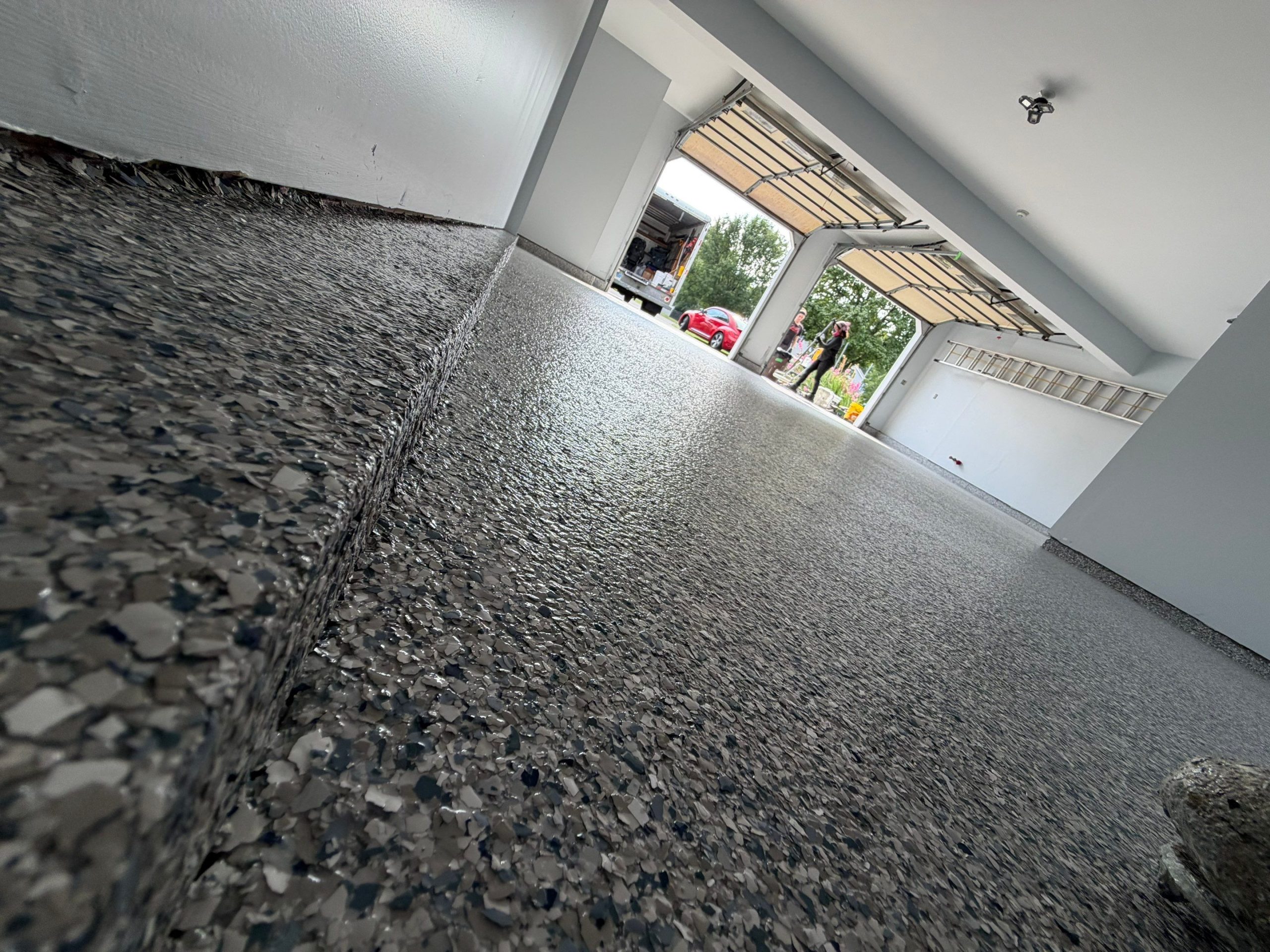 Close-up view of durable speckled epoxy flooring in a garage with open doors showing parked cars outside.