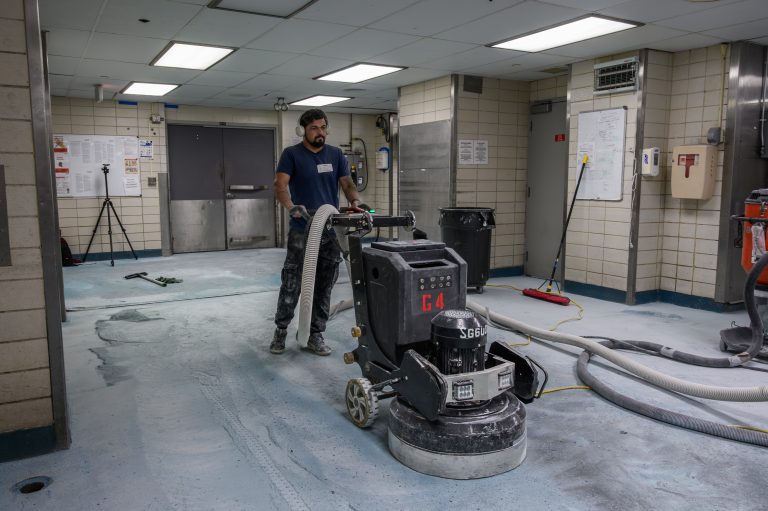 A worker uses a large floor grinder to polish a commercial concrete hallway.