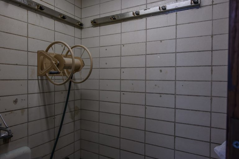 A hose reel is mounted on the white tiled wall of a utility room.
