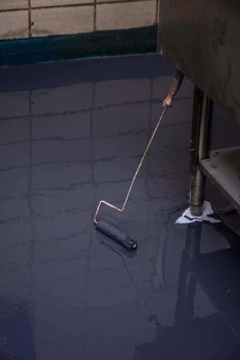A paint roller rests on a floor coated in wet gray epoxy resin.