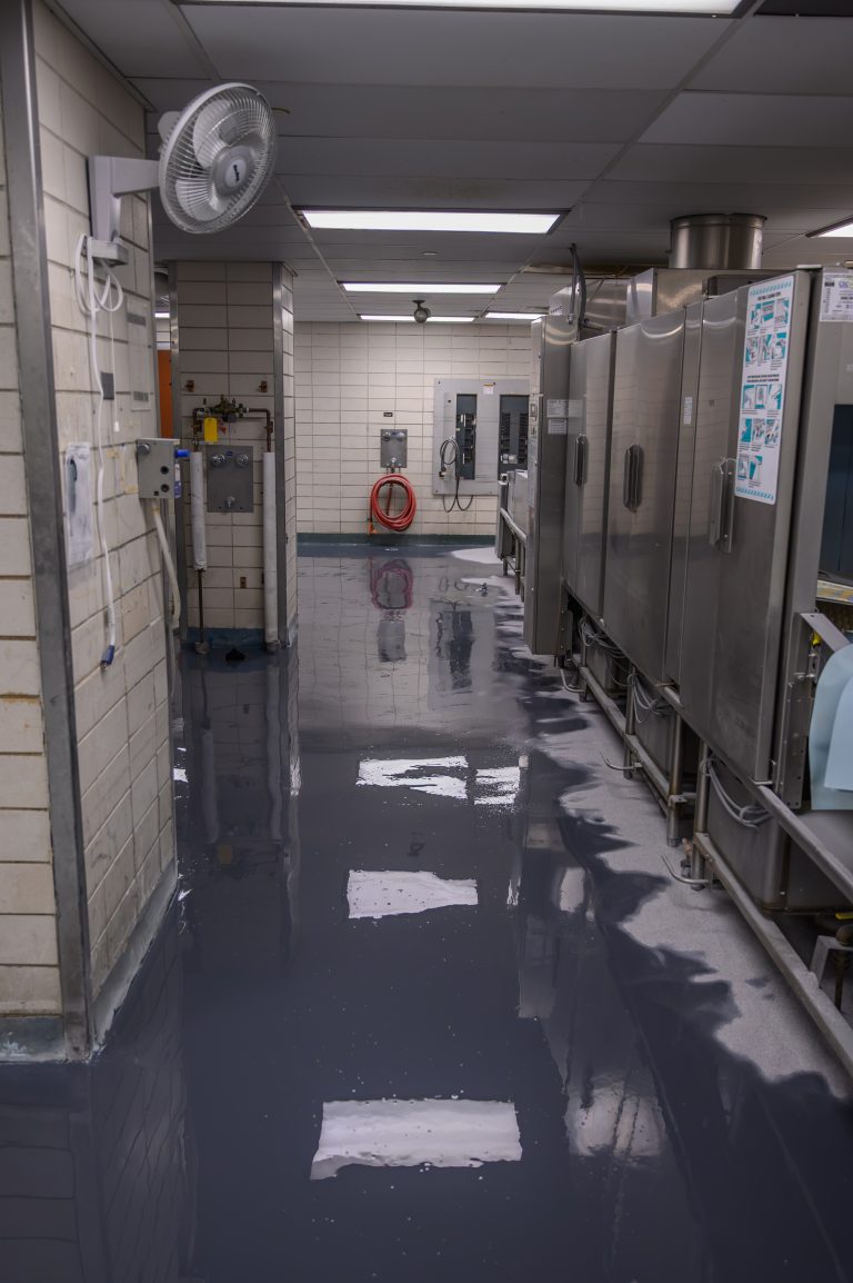 A freshly applied gray epoxy coating covers the commercial kitchen floor near stainless appliances.