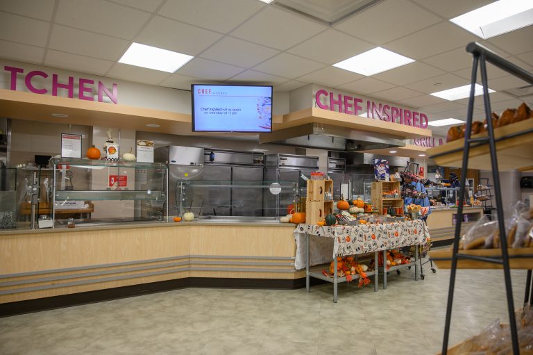 A cafeteria serving counter features autumn-themed decor and a sign reading Chef Inspired.