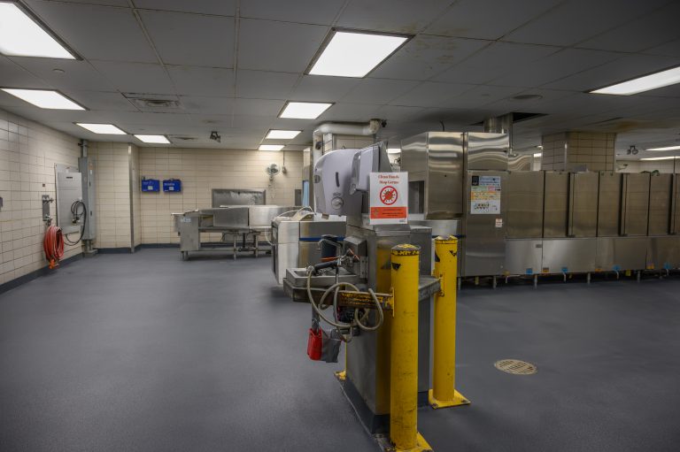 Commercial kitchen featuring stainless steel equipment, gray flooring, and a hand sanitizer station.