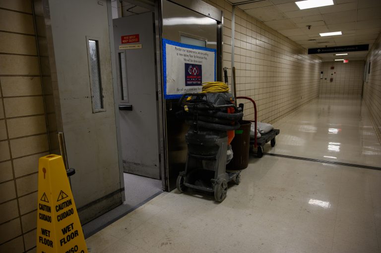 A floor cleaning machine and wet floor sign stand in a hallway beside a construction notice.