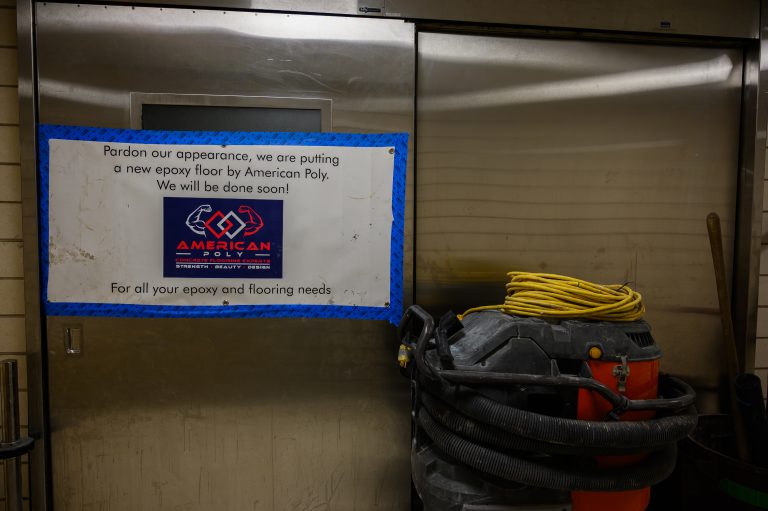 A sign on a metal door announces American Poly epoxy flooring next to a wet-dry vacuum.