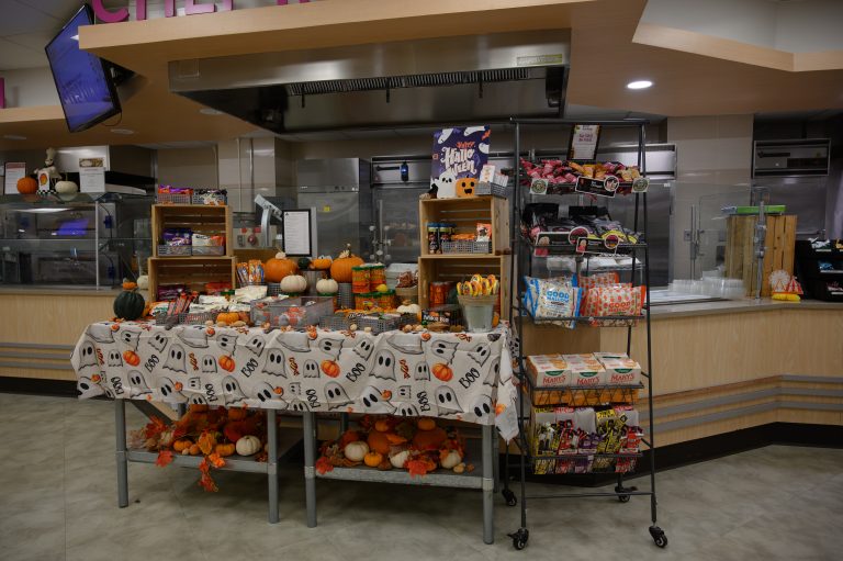A kitchen table with a Halloween-themed cloth, pumpkins, candy, and snacks.