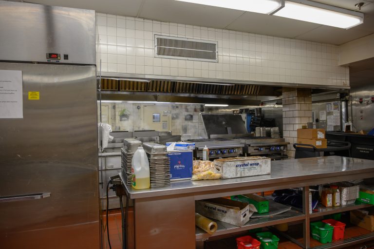 A commercial kitchen featuring stainless steel tables, a walk-in cooler, and food service supplies.