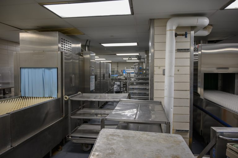 Industrial Hobart dishwashing machines and stainless steel prep tables in a commercial kitchen.